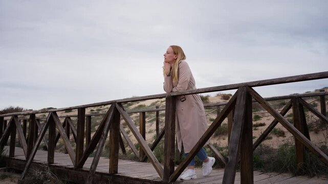 Woman stand on wooden pathway at beach, at transitional life moment, new chapter and change concept. Reflection, letting go, moving forward and quiet emotional transformation.