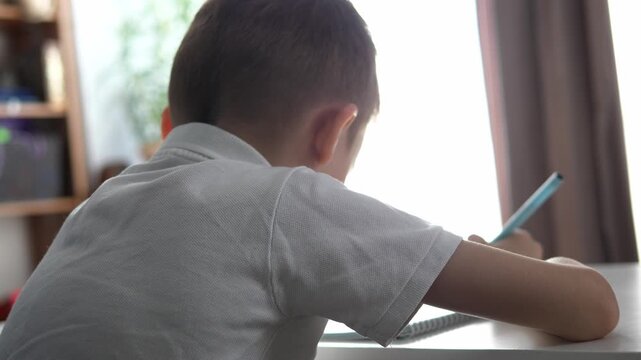 Close-up of a young boy writing or drawing with a pencil at a desk at home or school. Child focused on learning and doing homework. Concept of education, childhood development, concentration