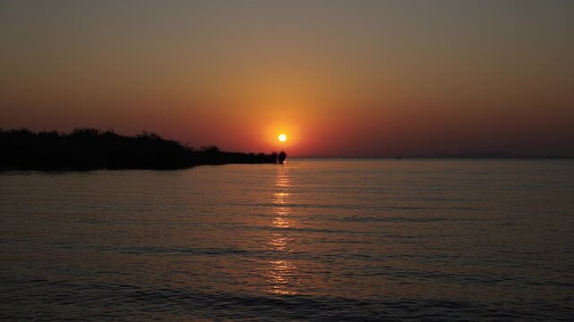 Golden sunset over the calm waters of Speke Bay at Lake Victoria, Tanzania, with silhouettes of the shoreline and distant hills.