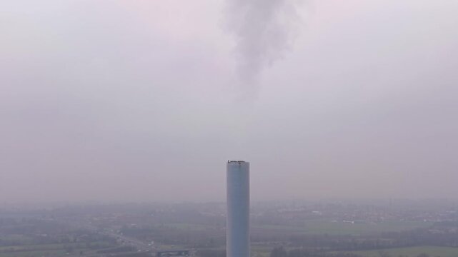 Industrial smokestack releasing smoke into foggy sky