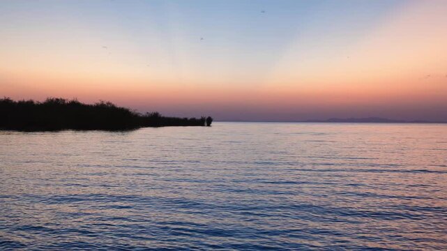 Golden sunset over the calm waters of Speke Bay at Lake Victoria, Tanzania, with silhouettes of the shoreline and distant hills.