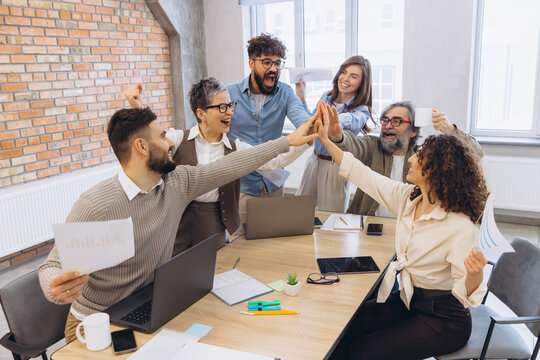 Diverse business team celebrating success in office, high fiving and cheering during a productive meeting