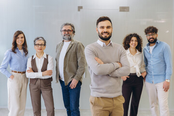 Fototapeta na wymiar Diverse business team smiling at camera in office, confident leader standing with arms crossed, representing collaboration and success