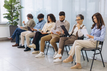 Fototapeta premium Diverse group of people in a waiting room, reviewing documents and resumes, anticipating their turn for a job interview