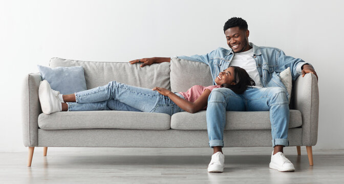 Free Time Together. Happy beautiful African American couple spending weekend resting on couch indoors at home in living room, relaxing and enjoying the company of each other, woman lying on man's lap
