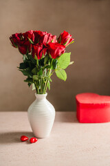 Obraz premium Valentine's Day festive background. Red roses flowers in a vase and heart gift box on the table. Festive greeting card, flat lay