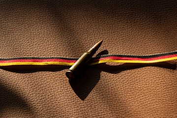 Naklejka premium A bullet rests on a ribbon in the colors of the German flag on brown leather for themes of defense, army, weapons, security