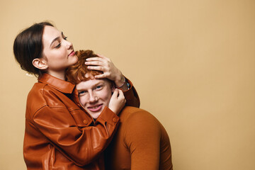 Young couple in warm brown clothing hugging each other on beige background with affection and love. Compassionate woman embracing smiling man in cozy outfits for relationship support.