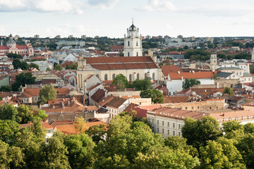 Fototapeta premium A panoramic roof-top view of Vilnius downtown cityscape. Red-tiled roofs, church spires, and historic buildings under sky.