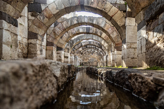 Low angle view of ancient Roman arches reflected in a water canal within the Agora of Smyrna, Izmir, Turkey. Historic stone masonry and architecture of an antique open-air museum.