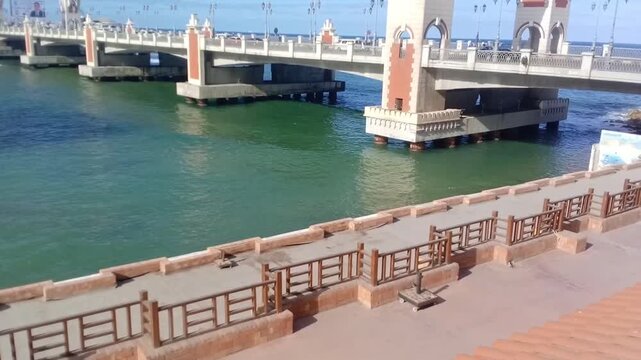 This is a great view of the Mediterranean Sea under Stanley Bridge. Some cars are running on the bridge. The bridge is on the Corniche Road in Alexandria, Egypt. It has a pedestrian walkway.