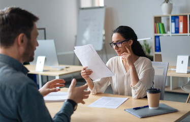 Fototapeta premium Personnel manager communicating with vacancy candidate, reading resume during job interview at office. Focused woman HR specialist studying applicant's CV. Headhunting and personnel recruitment