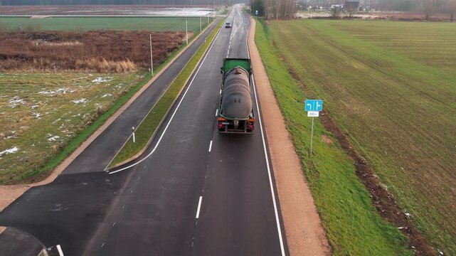 A large tanker truck travels down a countryside highway bordered by fields and a few patches of snow, under overcast skies. 26.09. 2025 Limbazi, Latvia