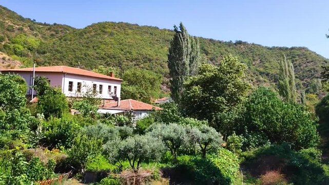 Scenic View of a Traditional Thracian Village with Red Tiled Roof Houses and a White Mosque Minaret Nestled in Lush Green Hills under Blue Sky, Rural Landscape of Northwest Turkey