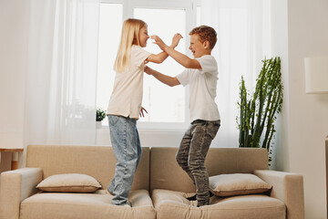 Two playful children jumping on sofa in bright living room, enjoying fun and energetic moment...