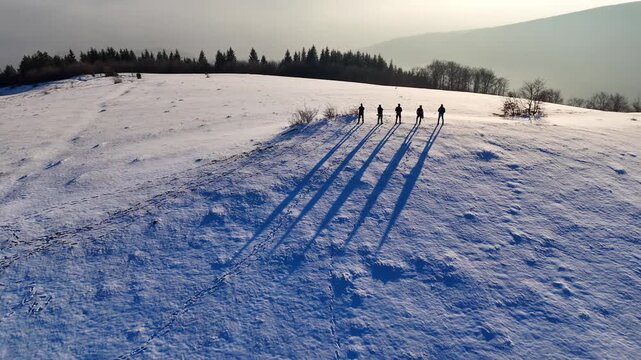 Drone shot of a winter landscape with snow and hikers standing on top of hill with valley fun of smog beneath them.