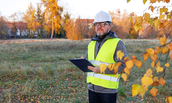 Matured male working on vacant field, new construction site. Environmental engineer or land surveyor conducting site inspection and territory analysis.