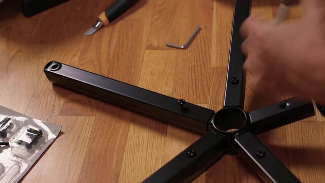 Hands assemble chair. Calm living room scene showing detailed furniture assembly process. Detailed tutorial on attaching casters and parts to chair base with precise technique