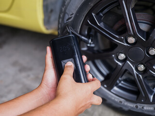 Obraz premium ​Close up of hands using a portable electric tire inflator to pump air into a car wheel. Modern automotive gadget for vehicle maintenance and emergency roadside assistance