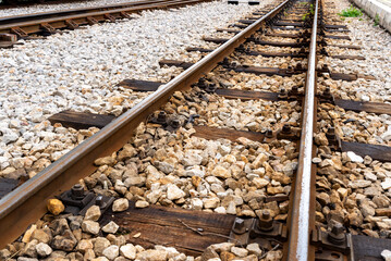 Naklejka premium Close up view of railway tracks with gravel and wooden sleepers, showing transportation infrastructure, rail construction details, and industrial background.