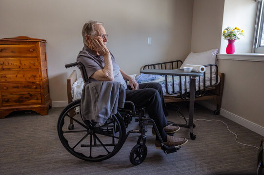 An old man sits in a wheelchair alone in a room. 