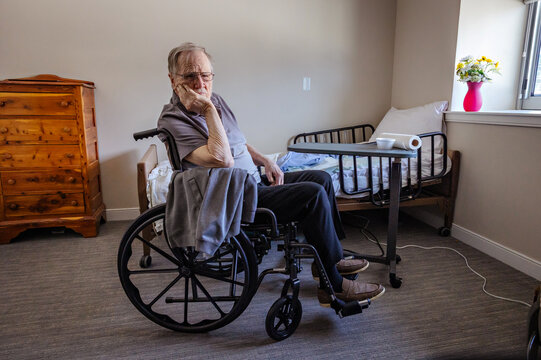 An old man sits in a wheelchair alone in a room. 