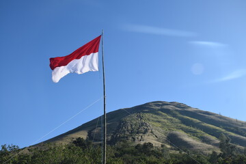 The red and white Indonesian flag against a backdrop of green hills and a blue sky.