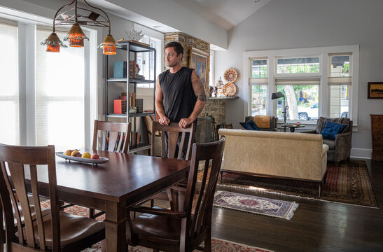 Young strong athletic man with tattoos at a dining room table inside a house. 