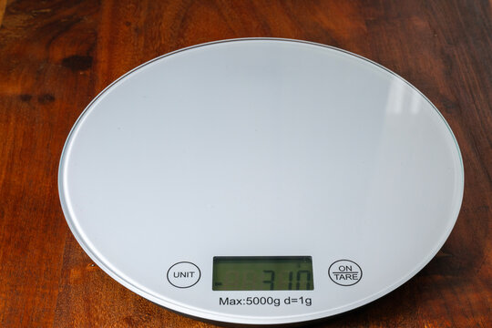 a sleek white digital kitchen scale displaying a weight of 310 grams on a wooden surface.