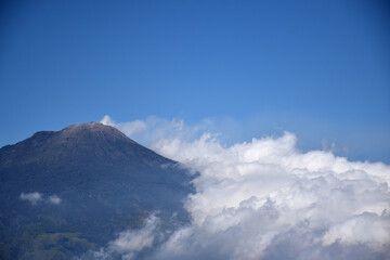 Fototapeta premium A mountaintop scene with white clouds enveloping it against a backdrop of a clear blue sky