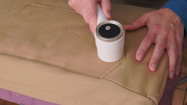 User carefully experiences lint removal on clothing in laundry space. Practical tutorial showcasing how to refresh garments using electric lint shaver in cozy setting