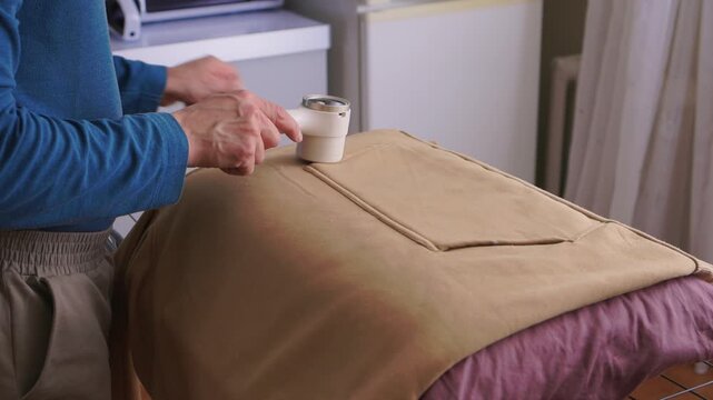 User carefully experiences lint removal on clothing in laundry space. Practical tutorial showcasing how to refresh garments using electric lint shaver in cozy setting