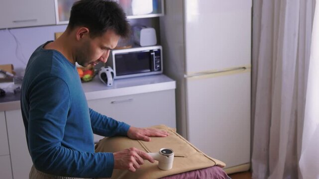 User carefully experiences lint removal on clothing in laundry space. Practical tutorial showcasing how to refresh garments using electric lint shaver in cozy setting