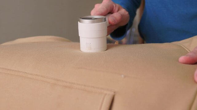 User carefully experiences lint removal on clothing in laundry space. Practical tutorial showcasing how to refresh garments using electric lint shaver in cozy setting