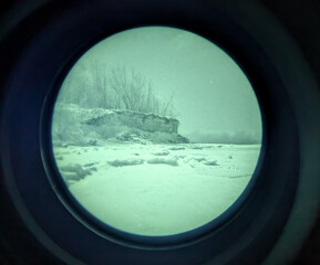 Winter maritime sea cliff and frozen shore viewed through authentic white phosphor night vision device for tactical coastal surveillance observation.
