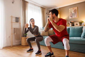 Obraz premium Active couple doing squats exercise while working out at home