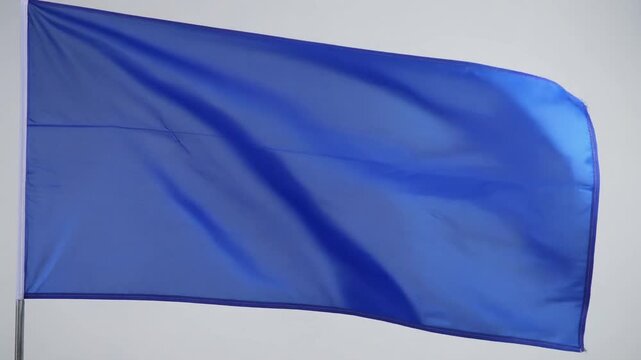 A simple, vibrant blue flag waves gently in the wind against a plain background, showcasing its solid color and flowing fabric