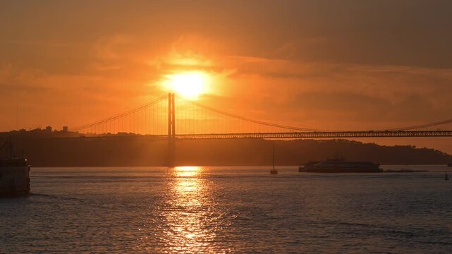 Sunset over 25 April Bridge in Lisbon Portugal by the water with boats and city in the background