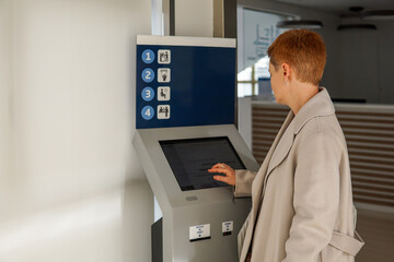 Middle aged woman taking queue ticket at reception desk in public service center, waiting for appointment
