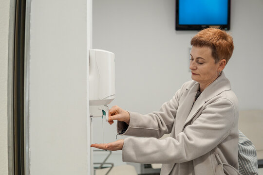 Middle aged woman taking queue ticket at reception desk in public service center, waiting for appointment