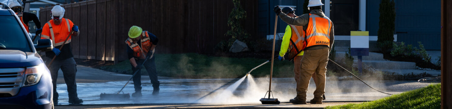 Specialized hazardous materials response team, hazmat cleanup of spilled chemicals on residential housing development job site, workmen with pressure sprayer and broom
