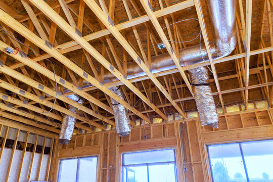 Wooden beams, ducts are inside house under construction, with over celling