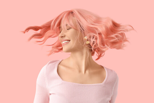 Beautiful young woman in pink wig on color background