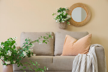 Fototapeta premium Interior of living room with sofa and blooming jasmine flowers near beige wall, closeup