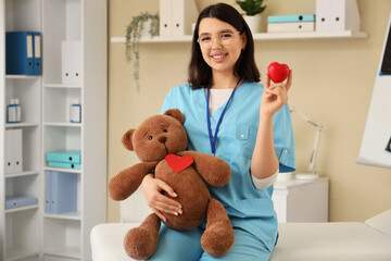 Female doctor with heart and toy bear in office. World Health Day