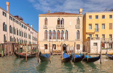 Naklejka premium Colorful historic buildings line the edge of a canal in Venice, Italy, with arched windows, balconies, and mooring poles.
