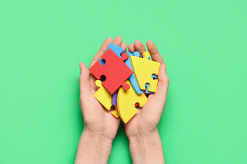 Fototapeta premium Female hands with colorful puzzle pieces on green background. Autistic disorder concept