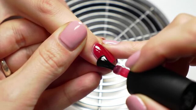 A hand applying red nail polish to a manicured nail