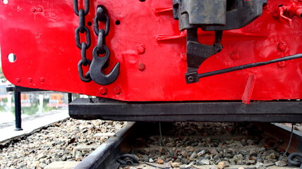 Close up of a red vintage locomotive coupling, chains, and wheels on railway tracks showing classic rail engineering.