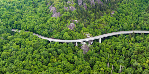 Road trip travel in Appalachian mountains. Car driving on Linn Cove Viaduct parkway through woods nature in summer wet rainy season. Colorful forest in North Carolina